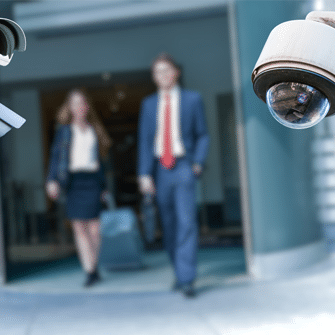 woman and man in business attire walking with a security camera on the foreground