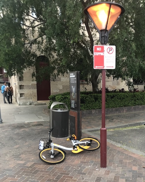 yellow bicycle lying on the sidewalk next to a No Stopping sign