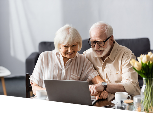 Smiling elderly couple using laptop near coffee cups on table